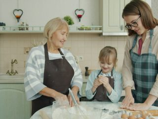 Happy family child, mother and grandmother are cooking baking and talking in kitchen concentrated on bakery. People, apartment and women concept.