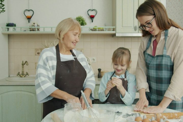 Happy family child, mother and grandmother are cooking baking and talking in kitchen concentrated on bakery. People, apartment and women concept.
