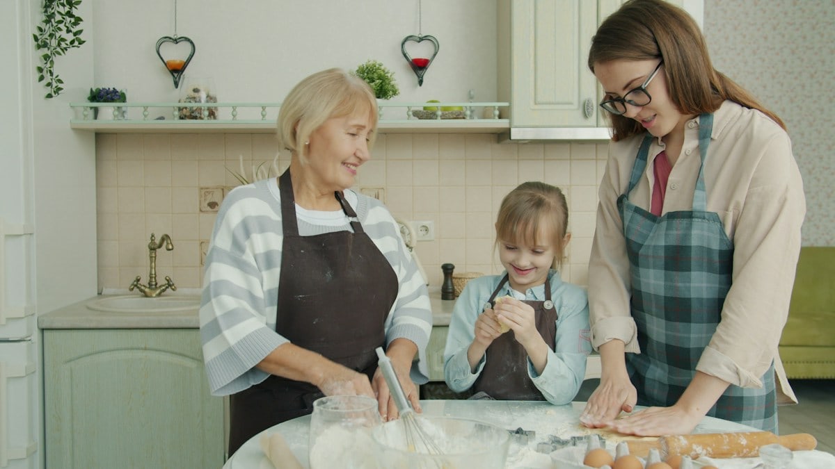 Happy family child, mother and grandmother are cooking baking and talking in kitchen concentrated on bakery. People, apartment and women concept.