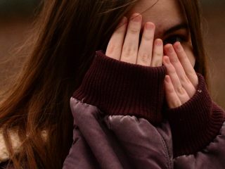 woman in purple sweater covering her face